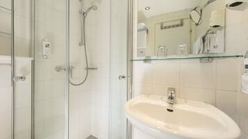 A modern bathroom with a glass shower enclosure, a white sink, and a glass shelf above the sink.