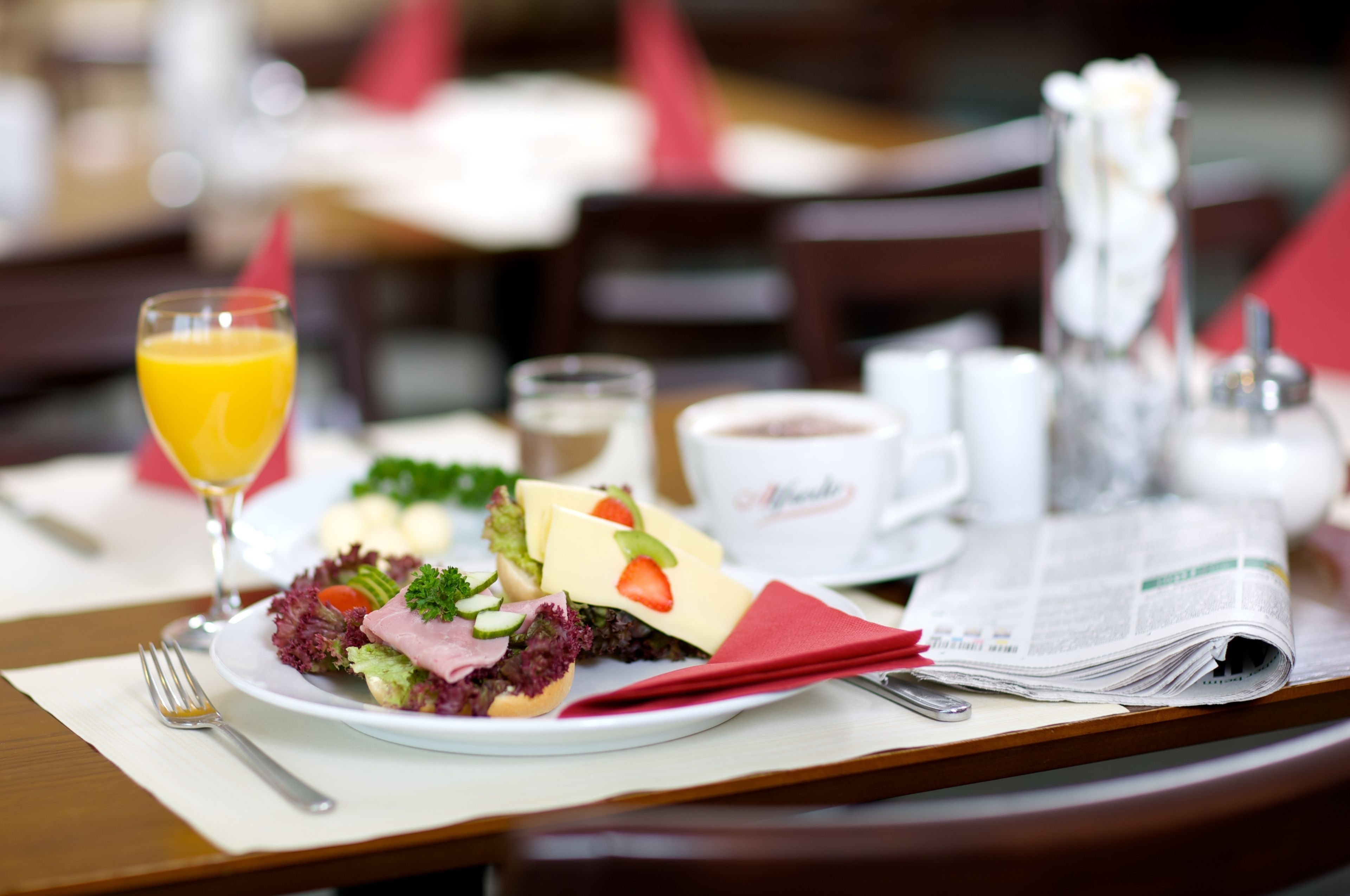 Ein Frühstückstisch mit Essen, Orangensaft, Kaffee und einer Zeitung.