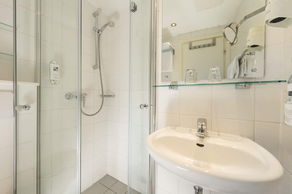 A modern bathroom with a glass shower enclosure, a white sink, and a glass shelf with toiletries.