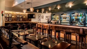 A bar area with wooden tables and chairs, a counter with bottles, and framed pictures on the wall. - AHORN Waldhotel Altenberg (Altenberg)