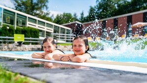 A swimming pool with two people lying on the edge, water splashing around them. - AHORN Waldhotel Altenberg (Altenberg)
