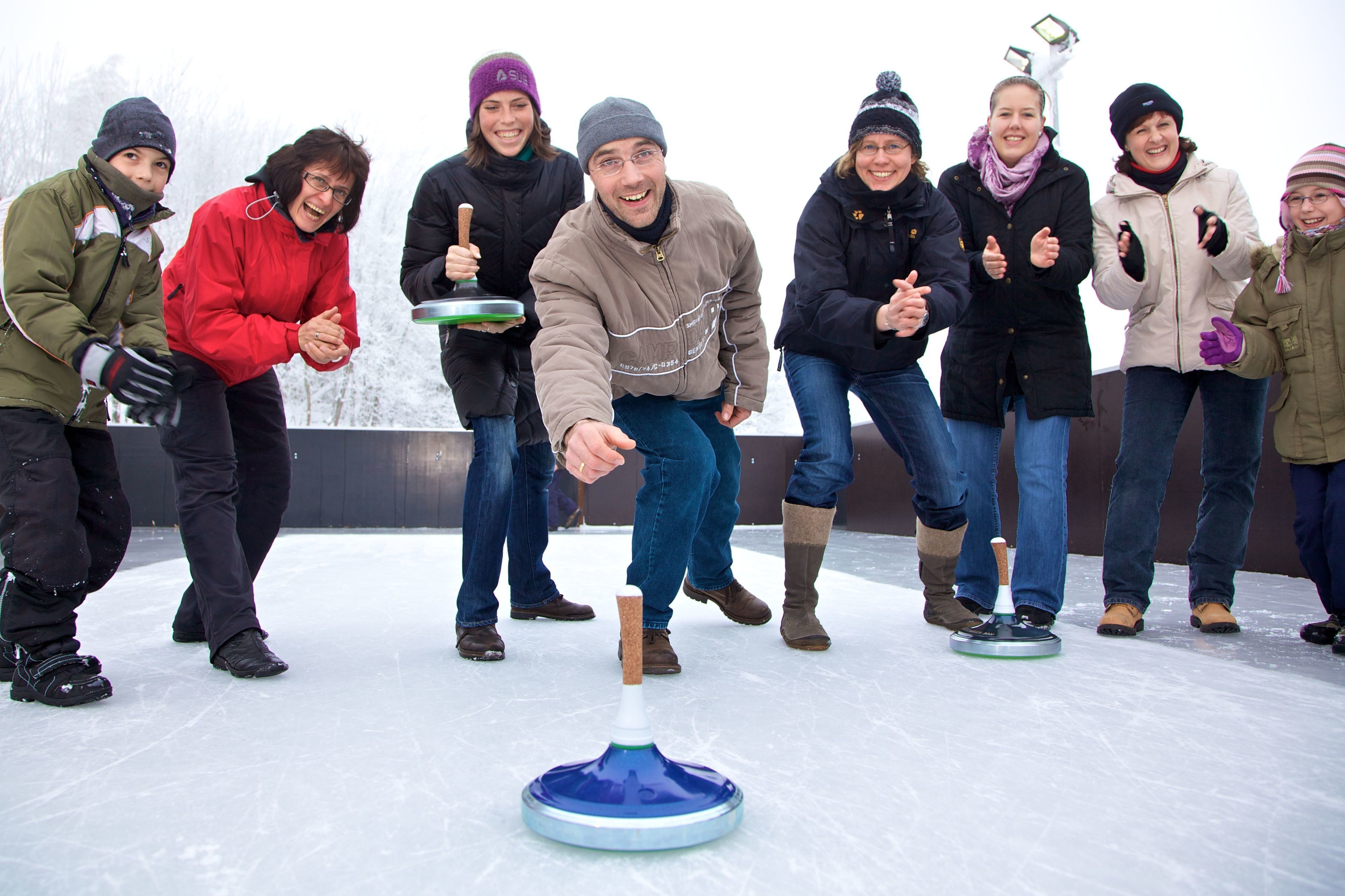 A group of people on an ice rink, some holding curling stones.