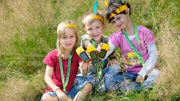 Three children sitting on grass, wearing headbands and holding yellow devices.