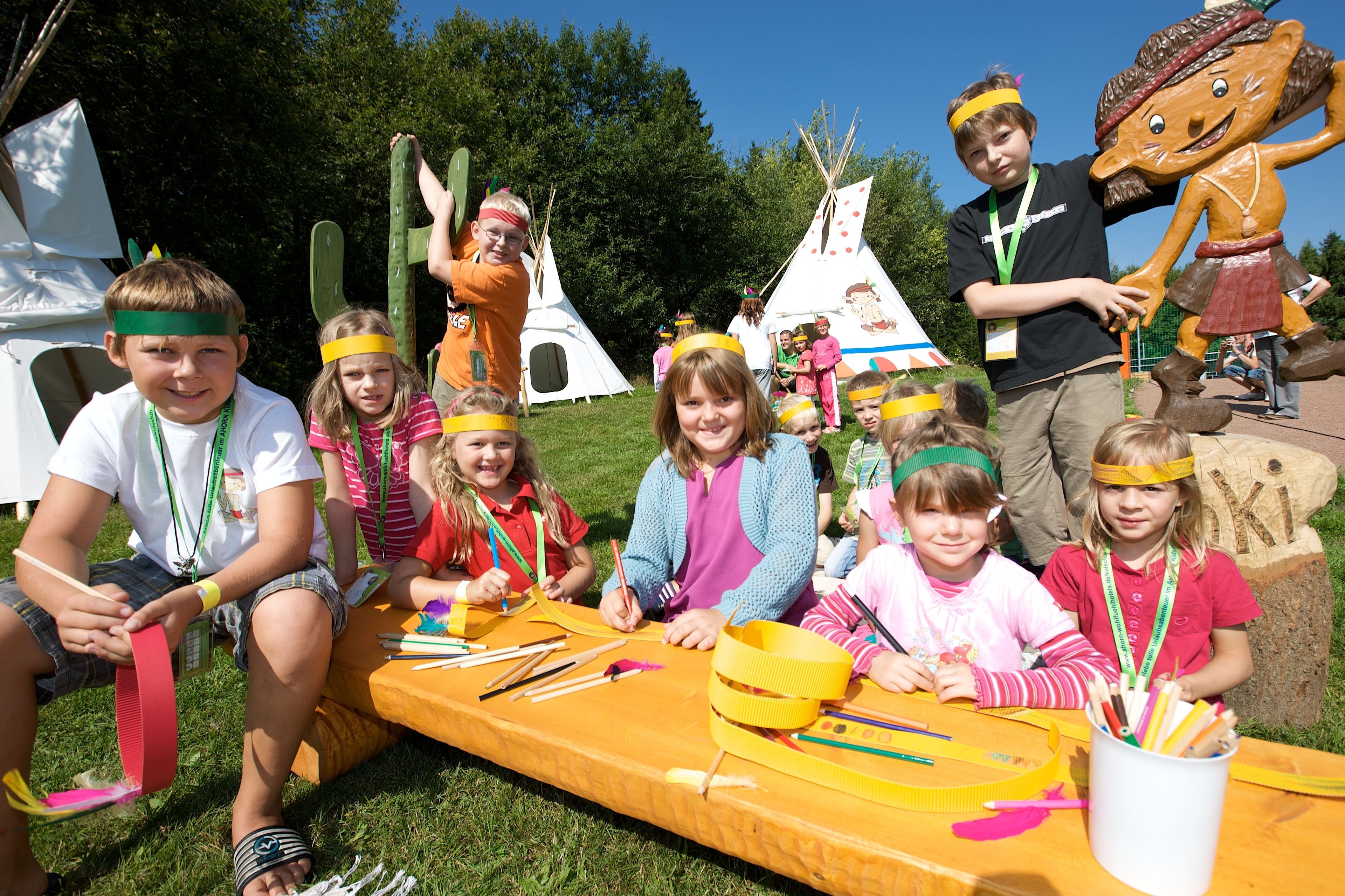 Un grupo de niños participa en una actividad al aire libre con material de manualidades sobre una mesa.
