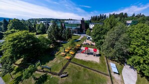 A modern building with a playground area, surrounded by trees and a clear sky. - AHORN Waldhotel Altenberg (Altenberg)