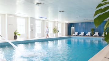 Ein überdachter Pool mit klarem, blauem Wasser, weißen Fliesen und einigen Liegestühlen.