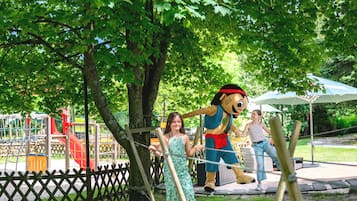 Un parque con un área de juegos, una valla de madera y un personaje mascota.