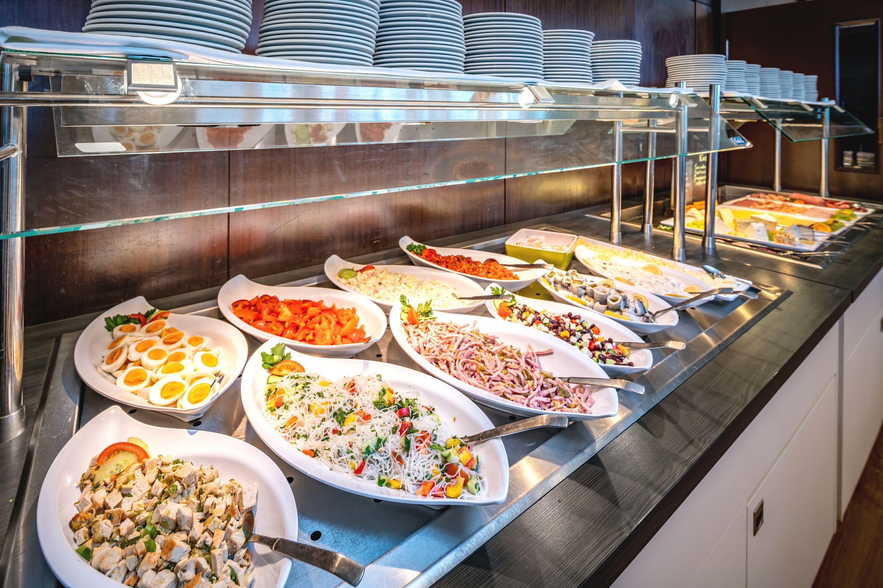 A buffet with various dishes, including salads, meats, and eggs, arranged on a stainless steel counter.