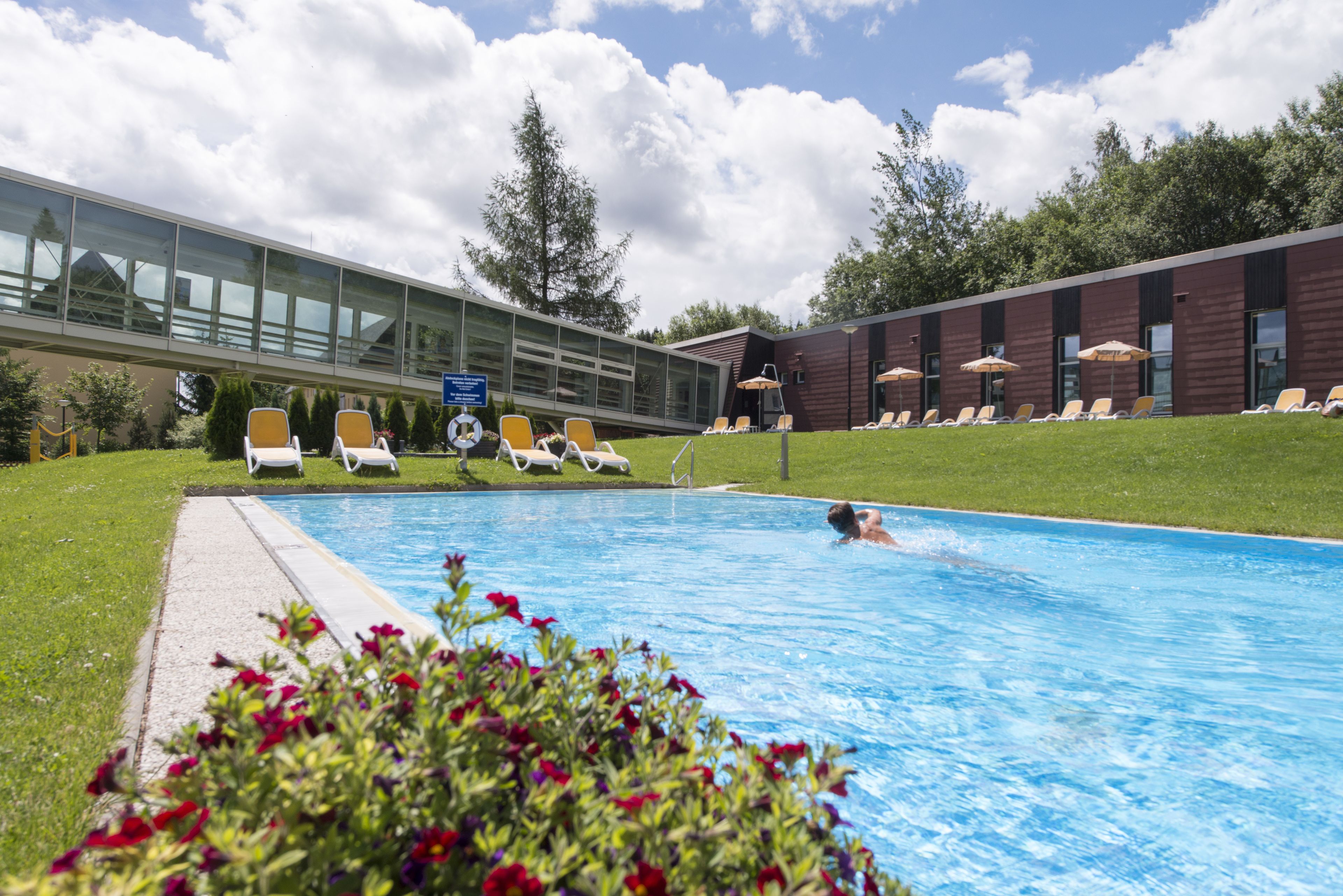 Una piscina con tumbonas y un edificio de amplios ventanales al fondo.