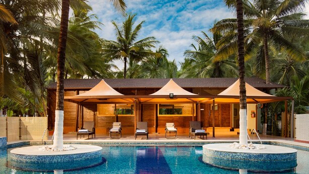 A pool area with two circular water features, lounge chairs, and umbrellas. - Sterling Anaikatti (Mannarkkad)