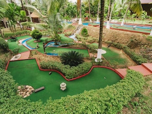 A miniature golf course with multiple holes, surrounded by lush greenery and palm trees.