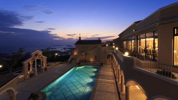 A swimming pool with a geometric pattern, a building with a balcony, and a view of the landscape.