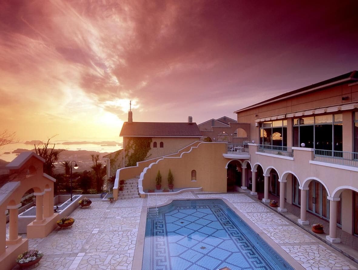 A pool area with a geometric tile design, a staircase leading to a balcony, and a sunset view.