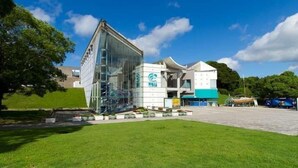 A modern building with a glass facade, a blue and white color scheme, and a spacious outdoor area with a lawn and a paved walkway.
