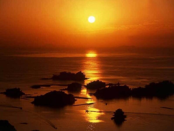 Un coucher de soleil sur une étendue d’eau calme, avec plusieurs petites formations terrestres au premier plan.