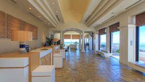 A spacious lobby with a stone floor, a reception desk, and large windows offering a view of the ocean.