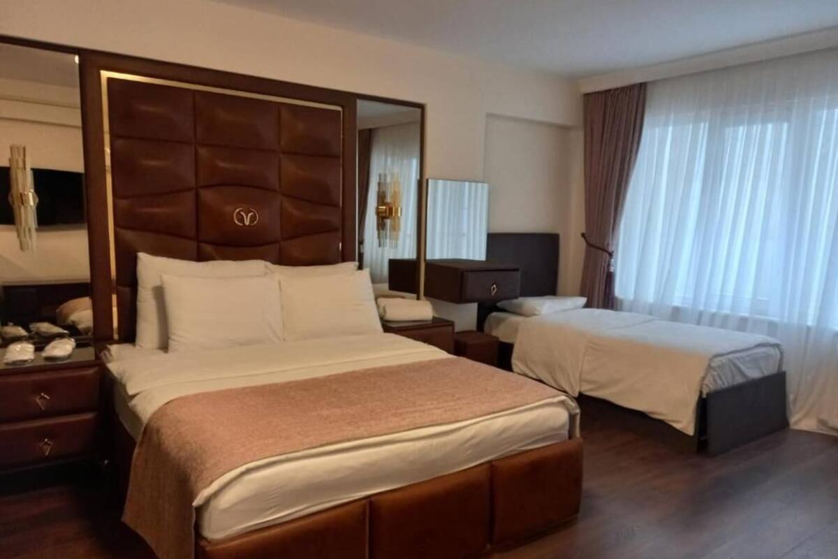 A hotel room with a large bed, a smaller bed, a nightstand, a dresser, and a mirror.