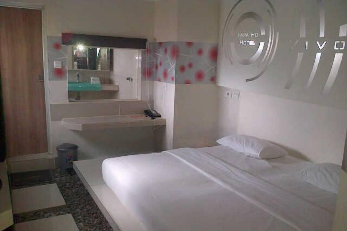 A hotel room with a bed, a small desk, a mirror, and a bathroom area.
