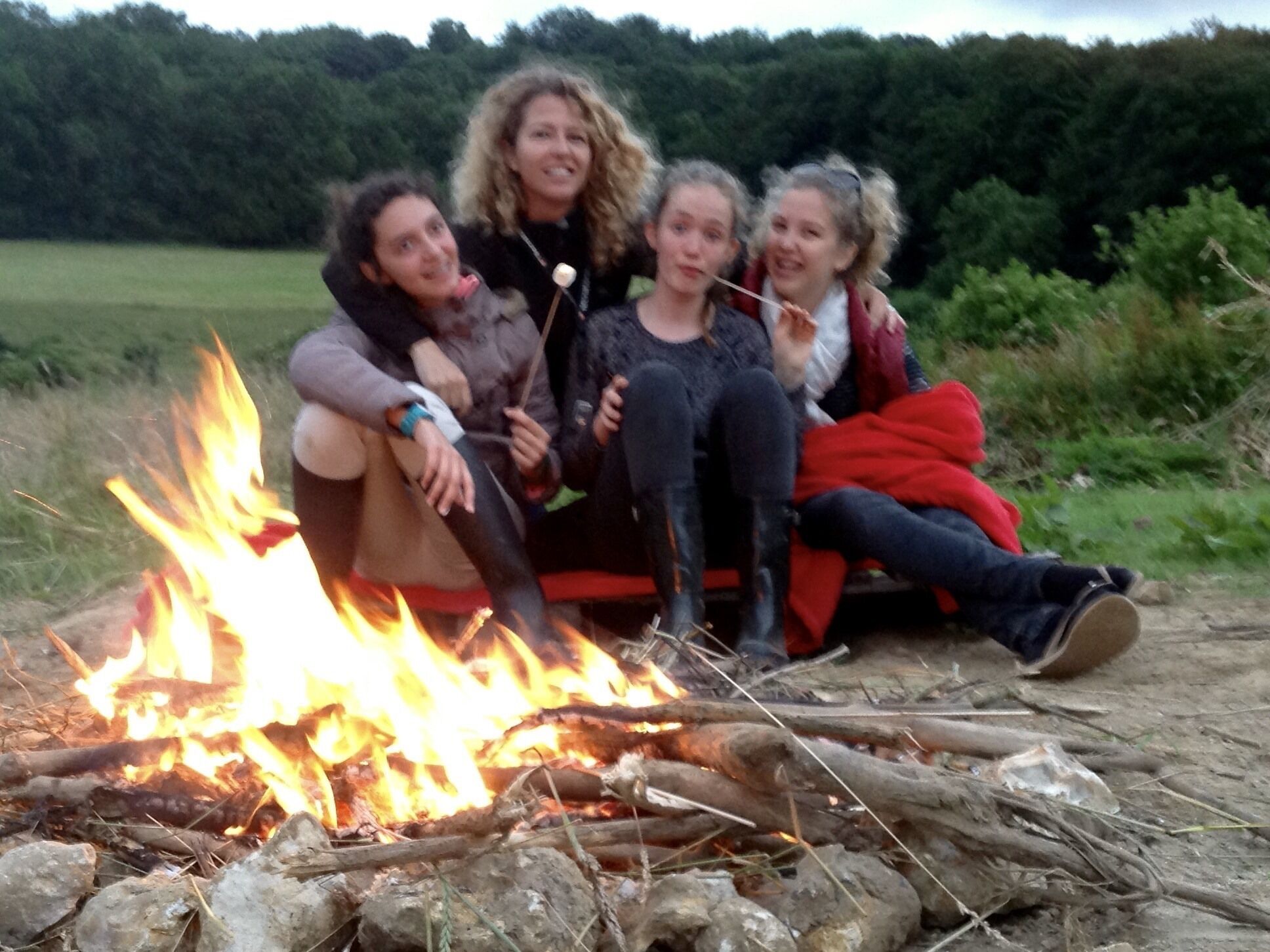 A group of people sitting around a campfire in an outdoor setting.