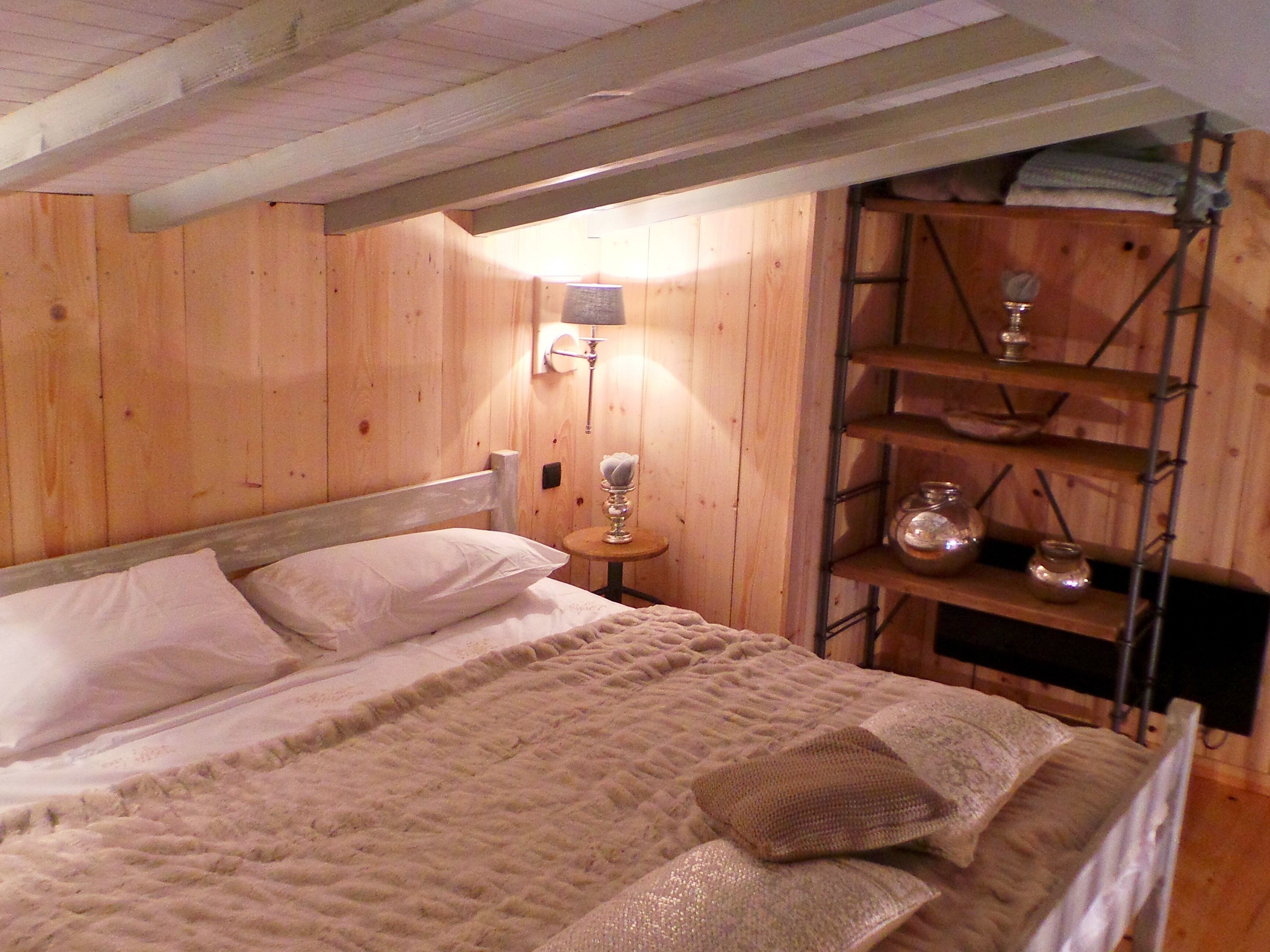 Une pièce en bois avec un lit, une table de chevet et une étagère où sont posés des bocaux.