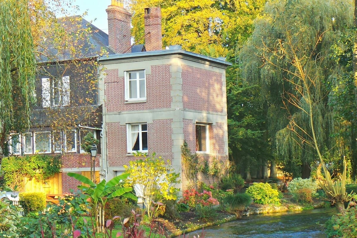 A two-story brick house with a garden and a small stream.