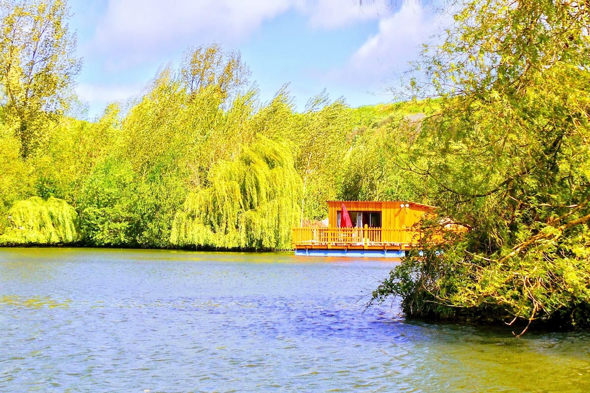 A wooden cabin with a balcony, surrounded by lush greenery and a calm lake.