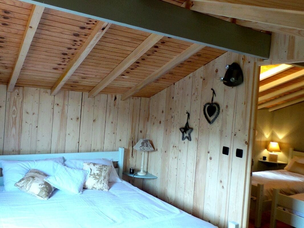 Dormitorio con paneles de madera, una cama, almohadas, una mesita de noche y decoración en la pared.