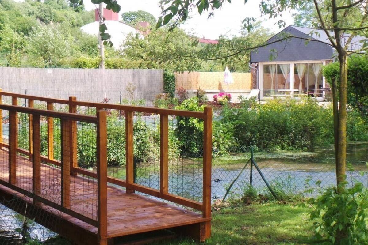 A wooden bridge over a pond with a house in the background.