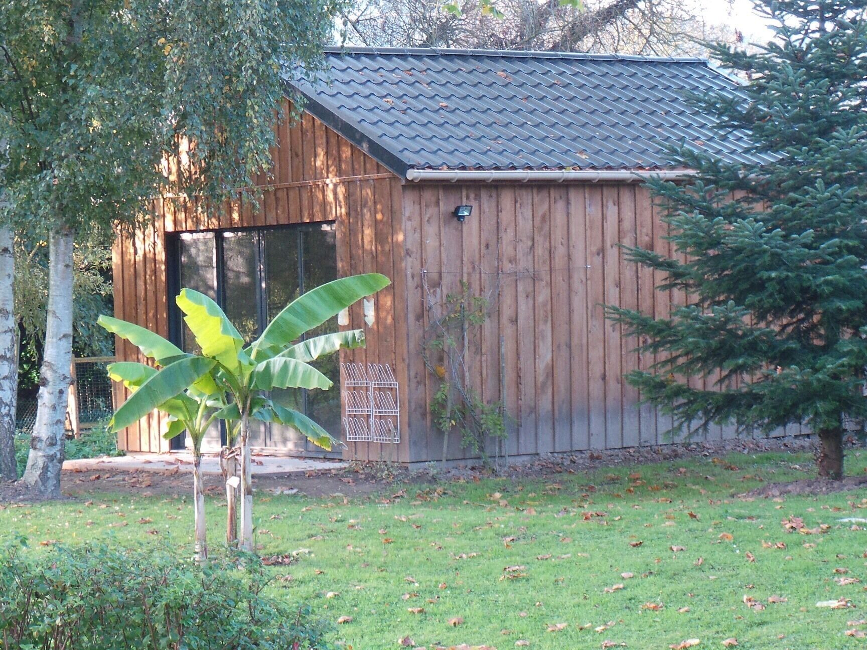 A wooden shed with a sloped roof, a metal door, and a small white security camera.