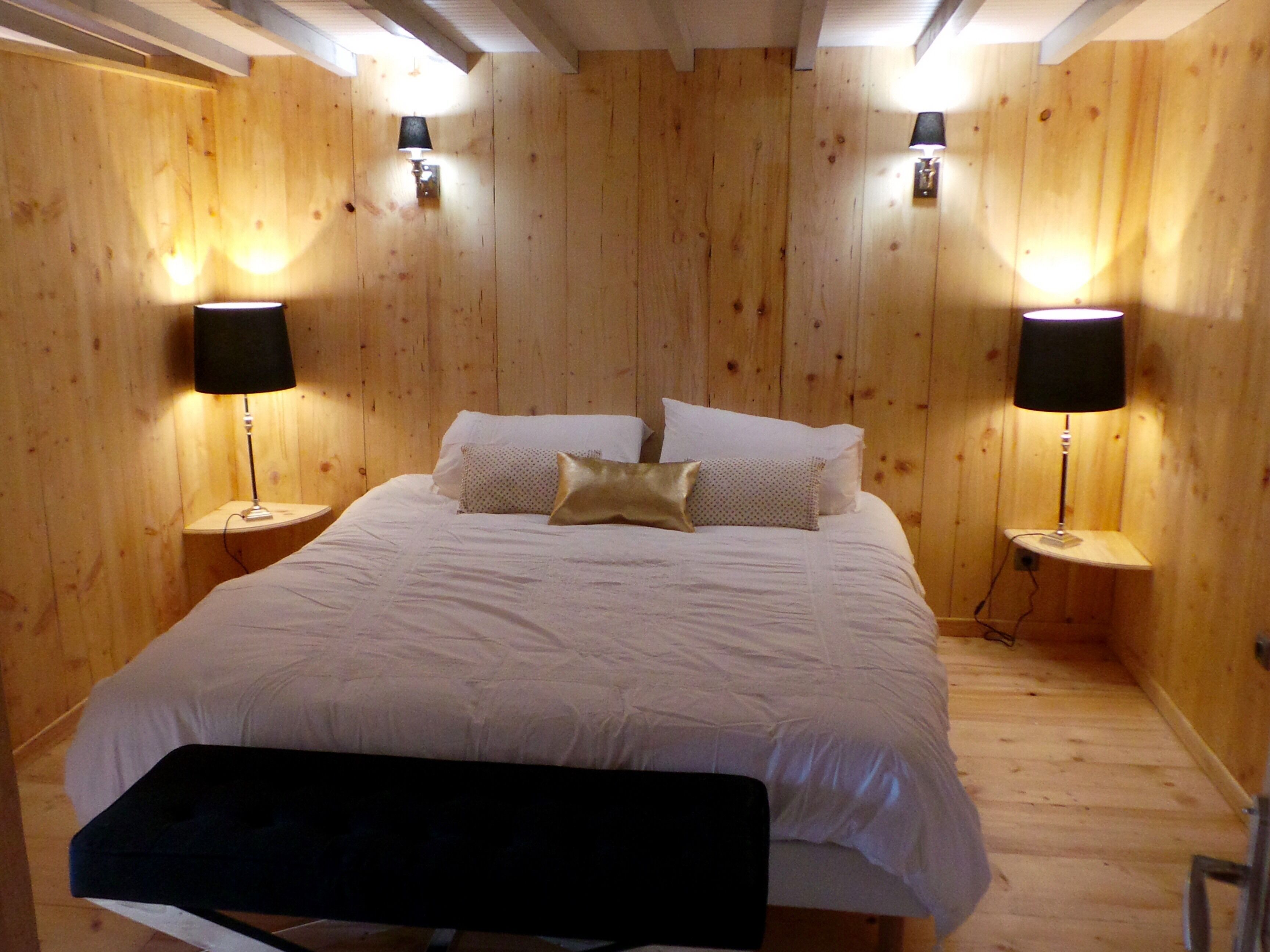 A wooden-paneled bedroom with a large bed, two bedside lamps, and a bench at the foot of the bed.