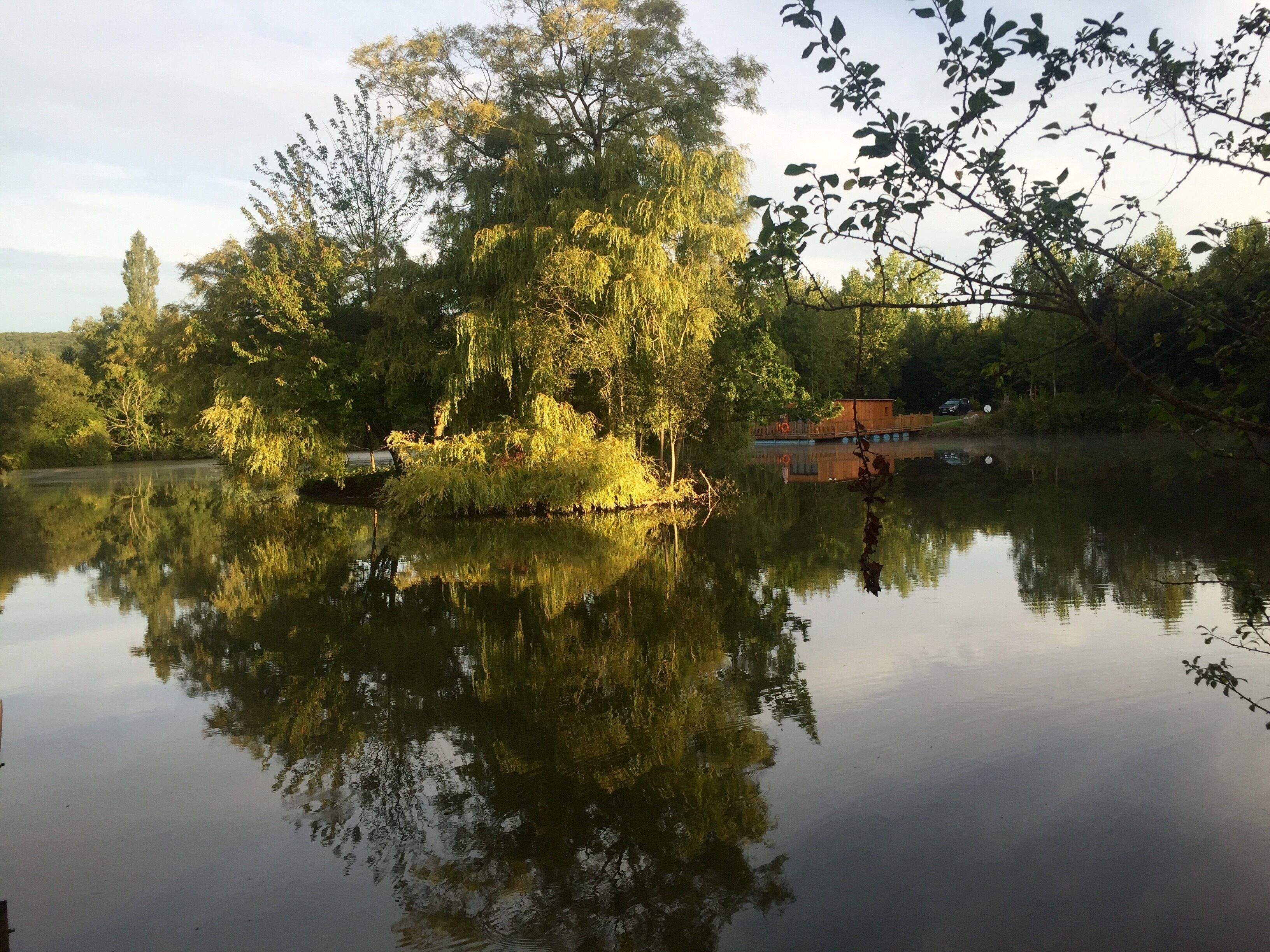 Un llac tranquil amb reflexos d'arbres i un edifici petit.
