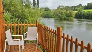 A wooden deck with two white chairs overlooking a calm river, surrounded by lush greenery and trees. - Au Fil de L'eau (Colleville)
