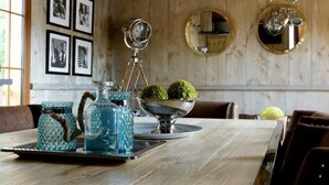 A dining area with a wooden table, framed pictures on the wall, and a chandelier. - Au Fil de L'eau (Colleville)