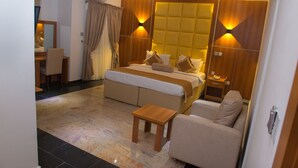 A modern hotel room with a large bed, a sofa, a small wooden table, and a desk with a chair.