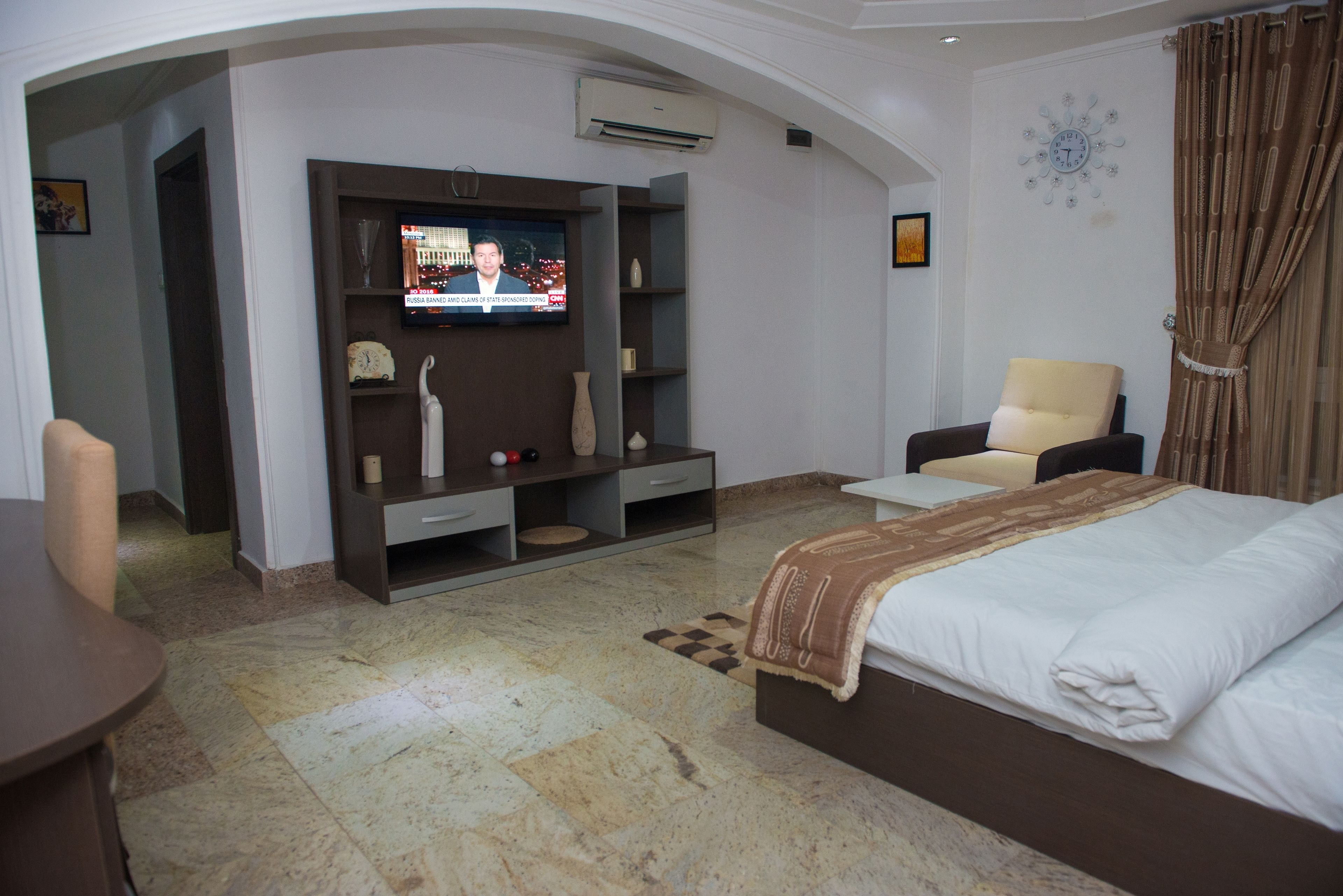 Quarto de hotel com cama, televisão, cadeira e escrivaninha.