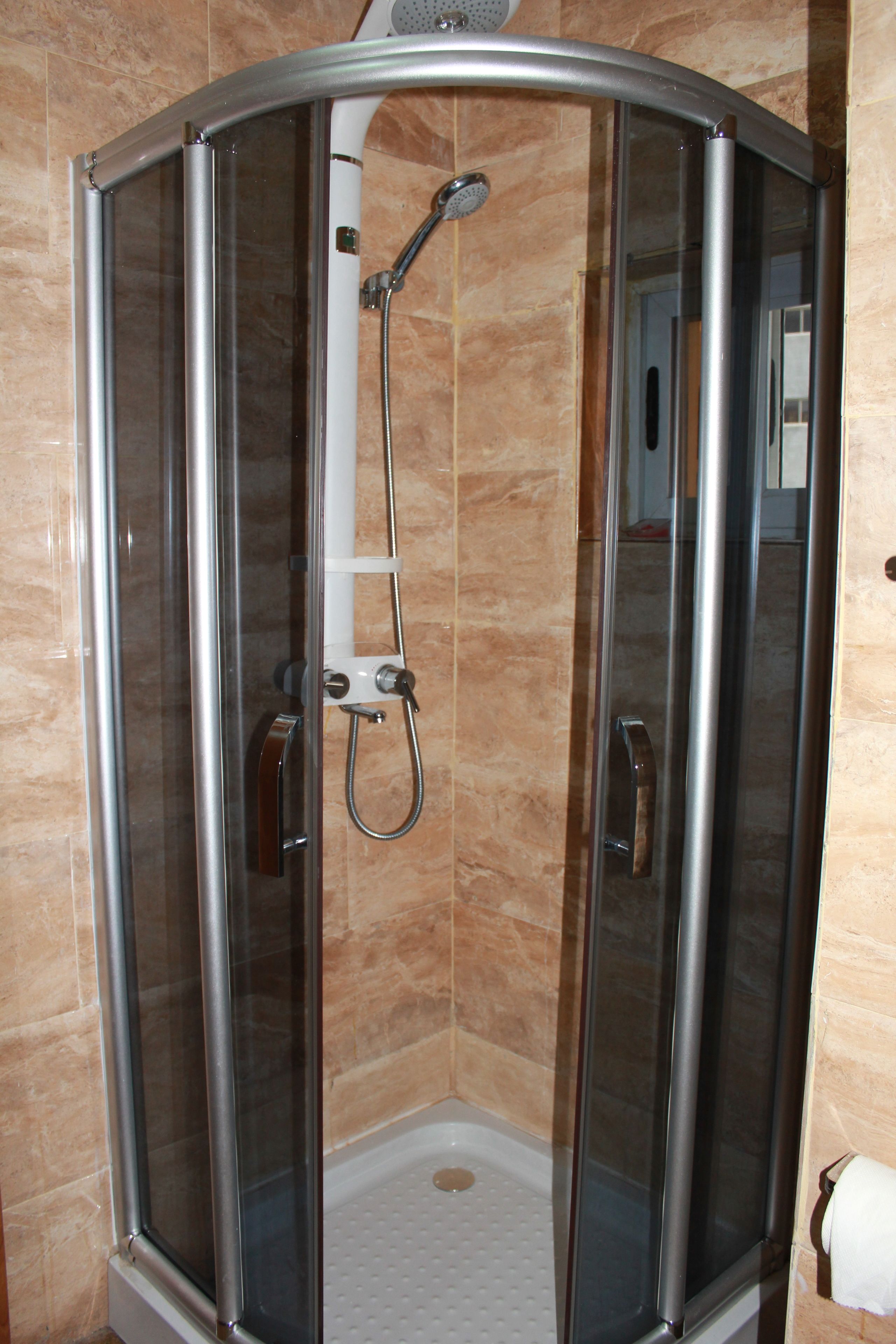 A glass-enclosed shower stall with a handheld showerhead and a handheld shower attachment.