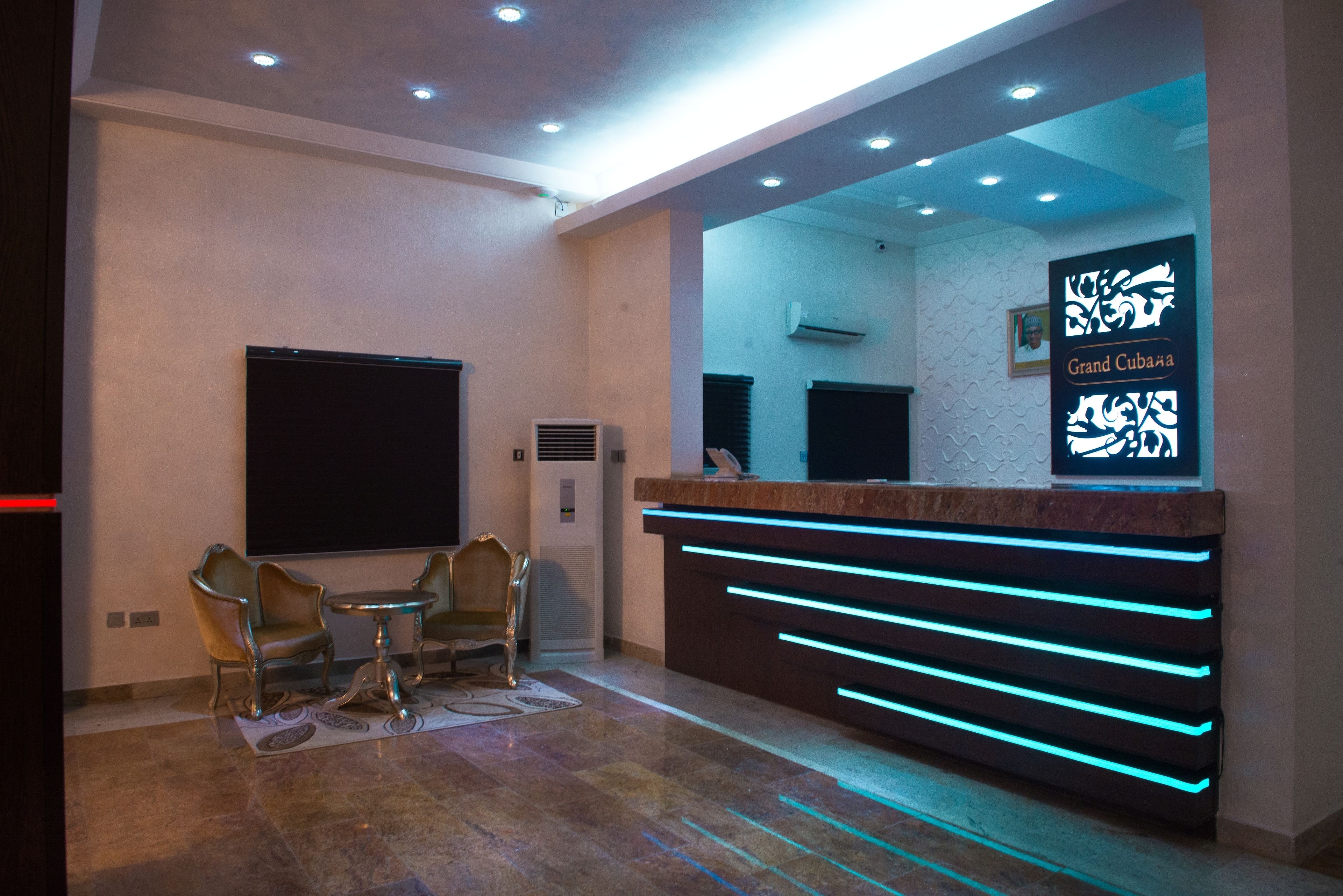 A reception area with a modern design, featuring a reception desk with blue LED lighting, a flat-screen TV, and two chairs.