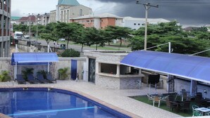 A swimming pool with lounge chairs, a covered patio area, and a view of surrounding buildings.