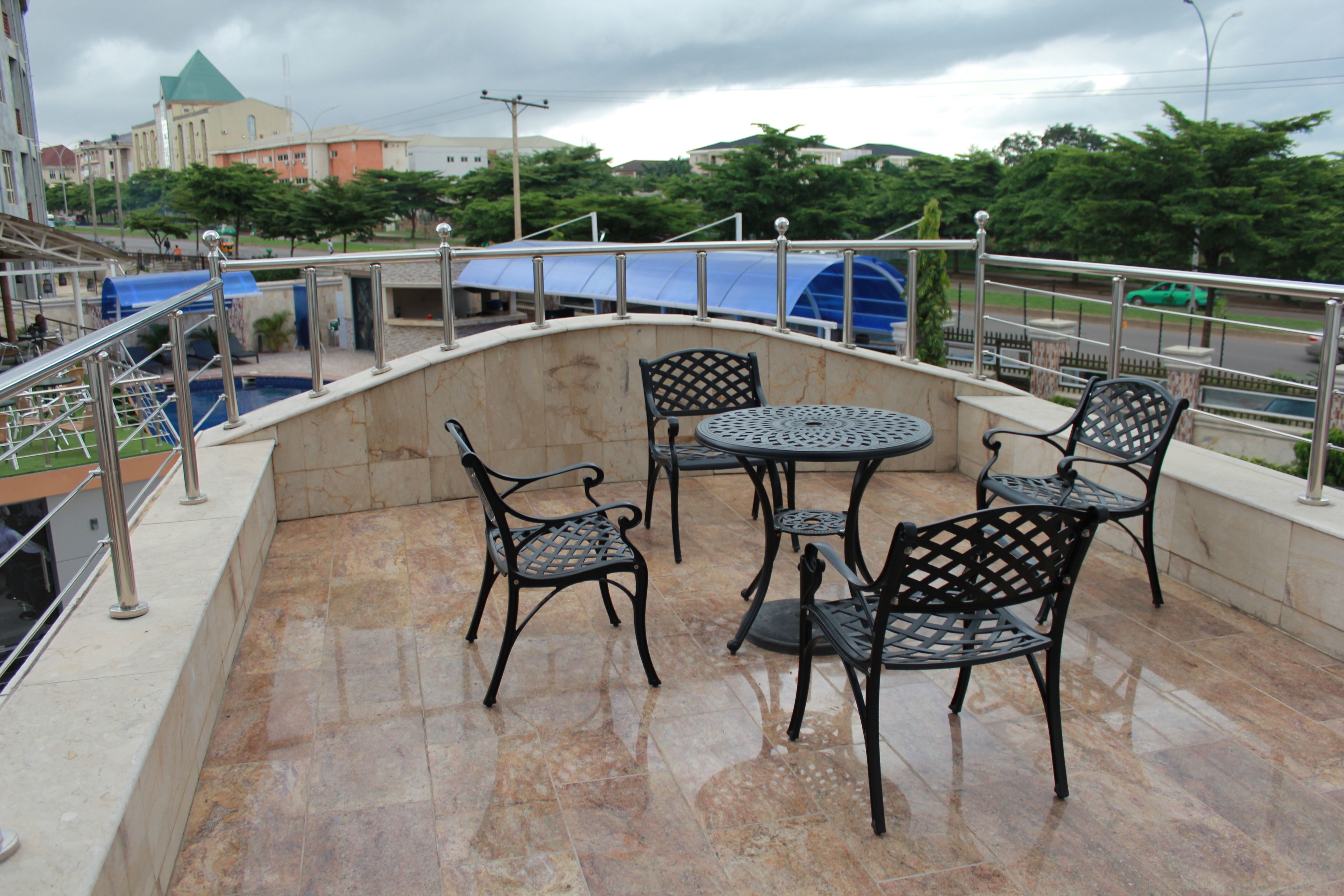 A terrace with a stone wall, metal railing, and outdoor furniture including chairs and a table.