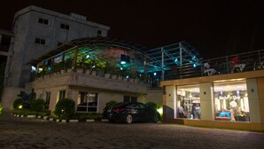 A building with a glass structure on the upper level, a parked car, and a storefront with a barber shop.