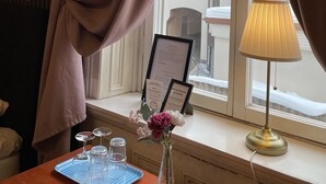 A hotel room with a window, curtains, a table with a vase of flowers, a lamp, and a menu on the windowsill. - Hotell Sta Clara (Sundsvall)