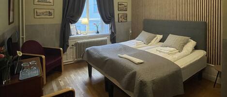 A modern hotel room with a large bed, a chair, a desk, and a window with curtains.