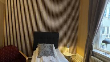 Une chambre d’hôtel avec un lit, une chaise, une lampe et une fenêtre avec des rideaux.