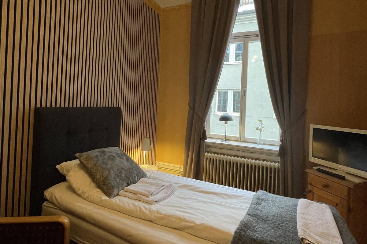 Una habitación de hotel con una cama, una silla, un televisor y una ventana con cortinas.