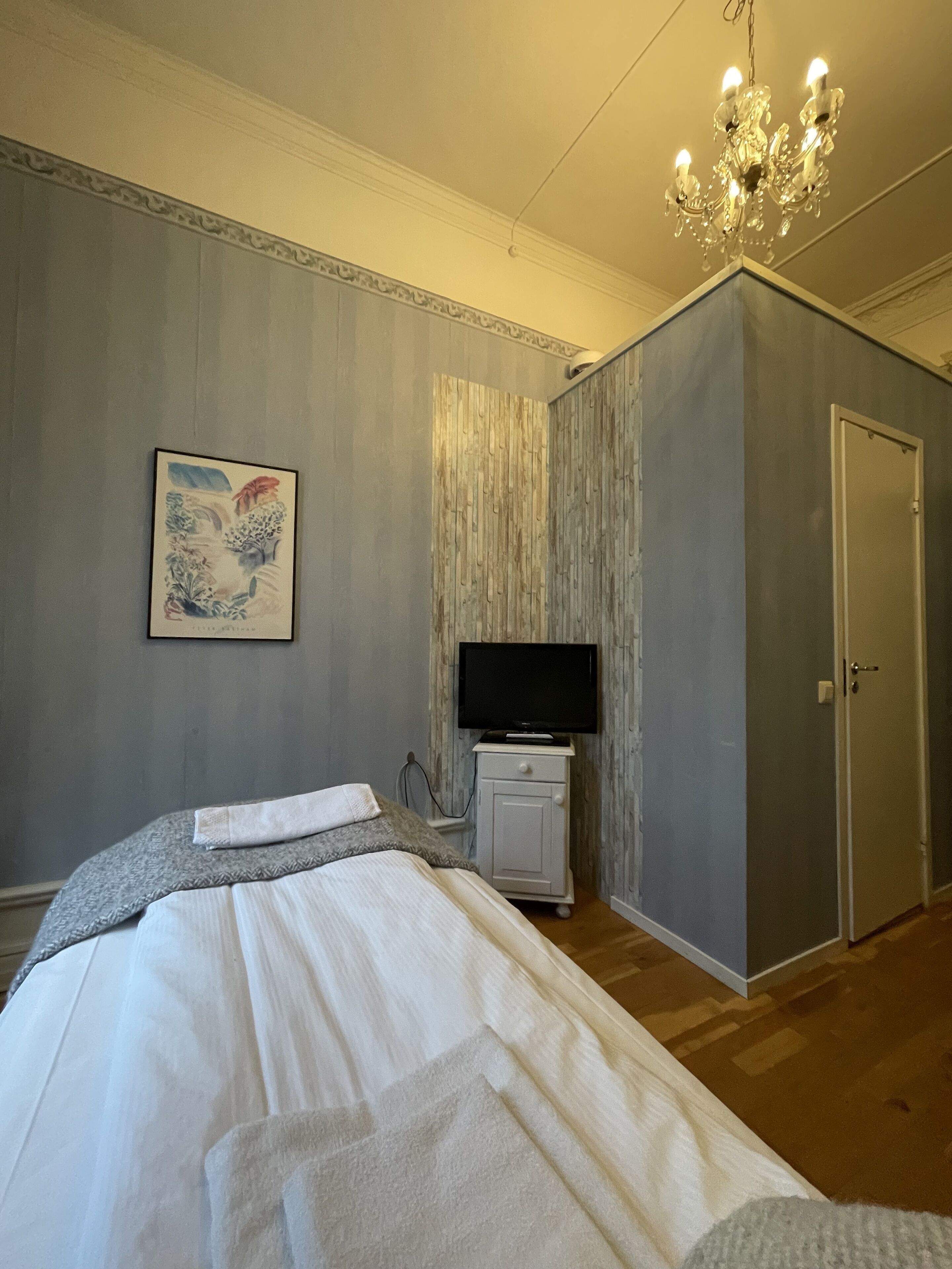 A bedroom with a bed, a TV on a stand, a door, and a chandelier.
