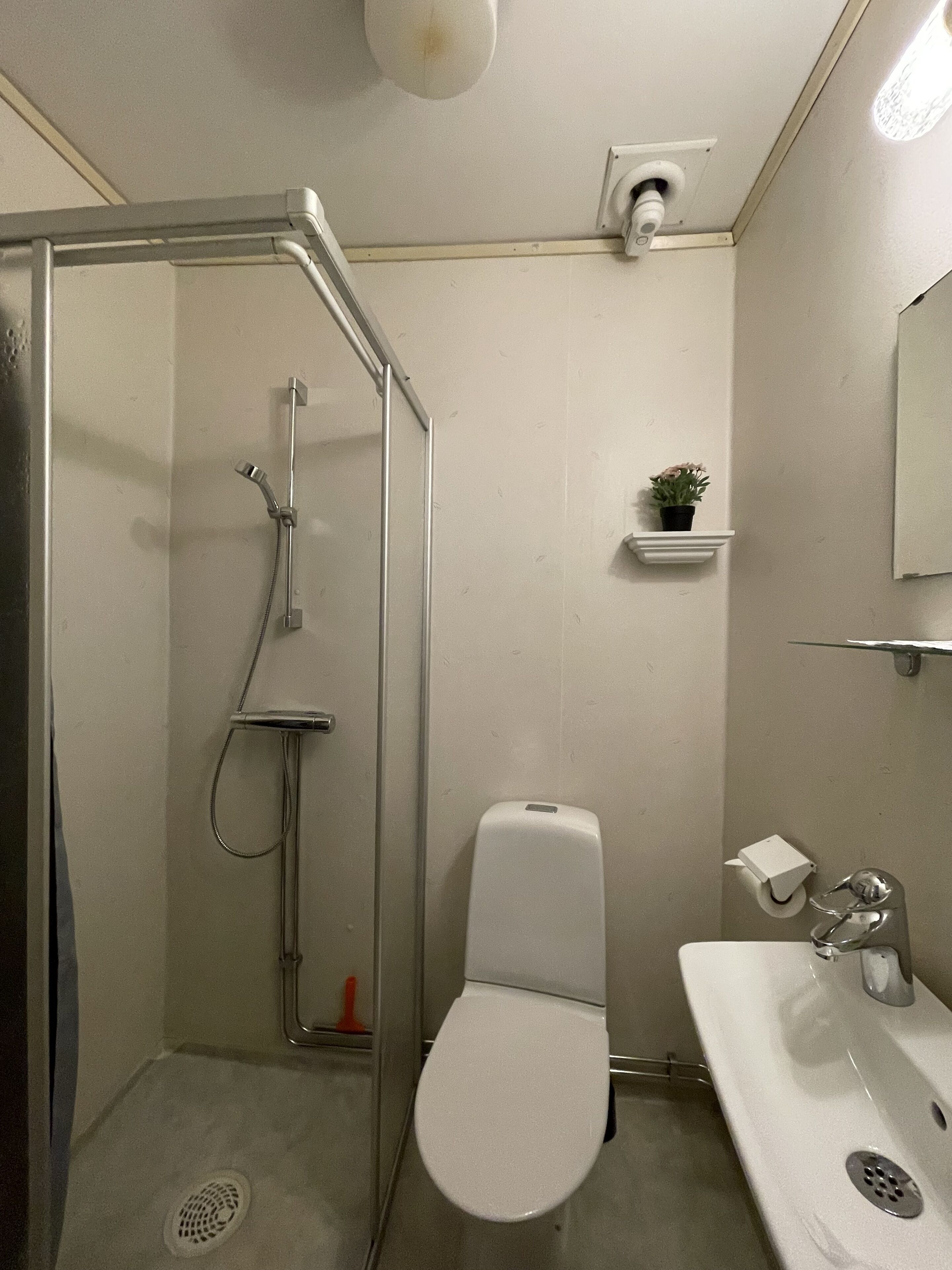 Un baño con ducha separada por mampara de vidrio, inodoro y lavamanos.
