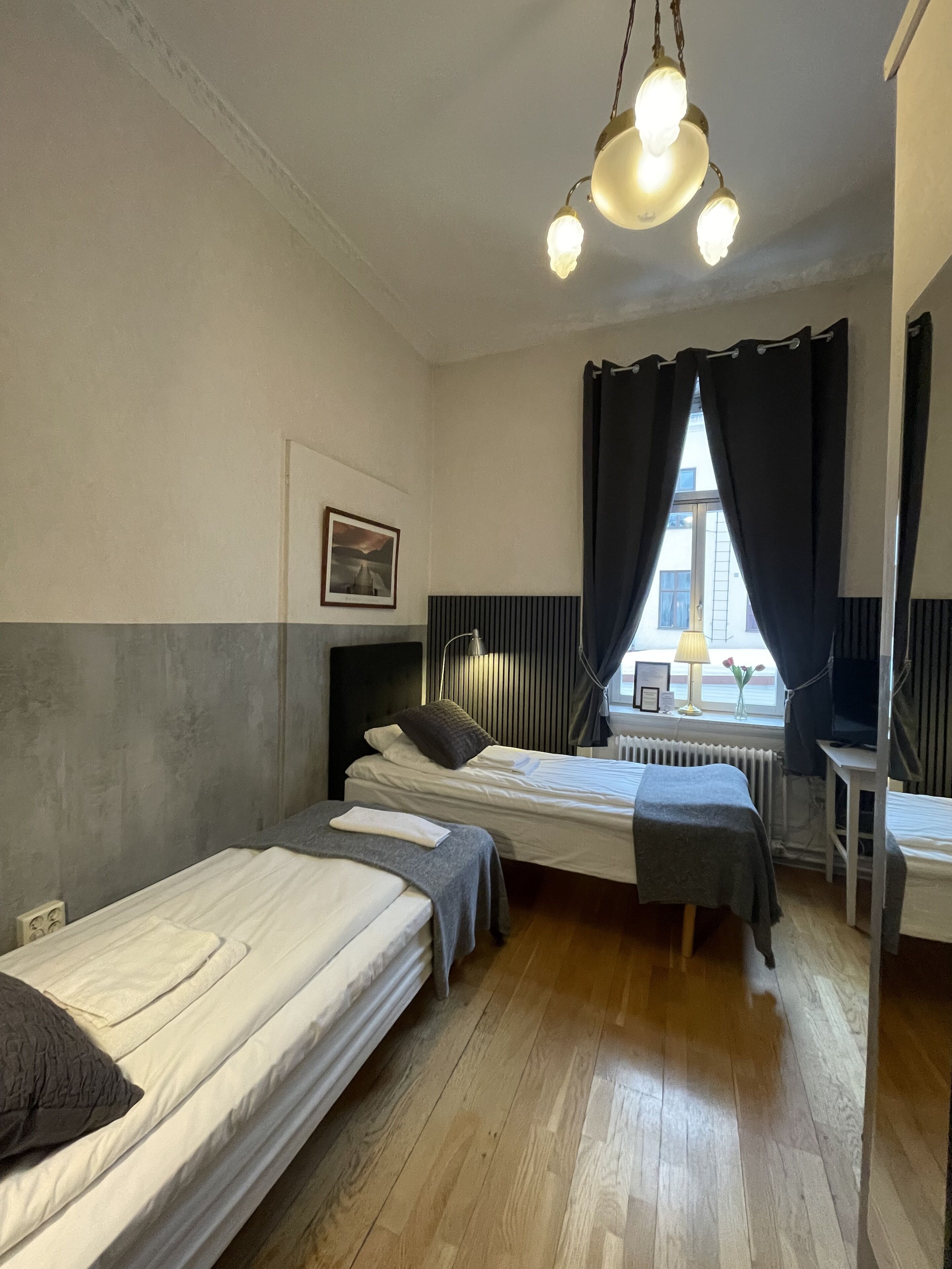 A room with two beds, a desk, a radiator, and a window with curtains.