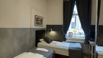 Ein Zimmer mit zwei Betten, einem Schreibtisch, einem Heizkörper und einem Fenster mit Vorhängen.