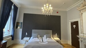 A hotel room with a large bed, a chandelier, a desk, and a chair. - Hotell Sta Clara (Sundsvall)