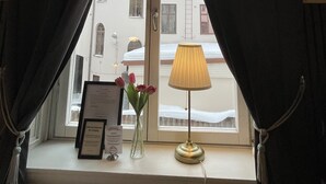 A window with curtains, a lamp, a vase with flowers, and a framed sign on a windowsill. - Hotell Sta Clara (Sundsvall)